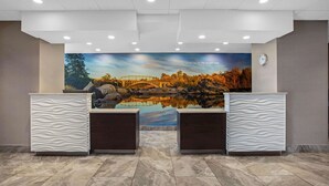 Un área de recepción con un mural de un puente y árboles, dos mostradores de recepción y un reloj en la pared.