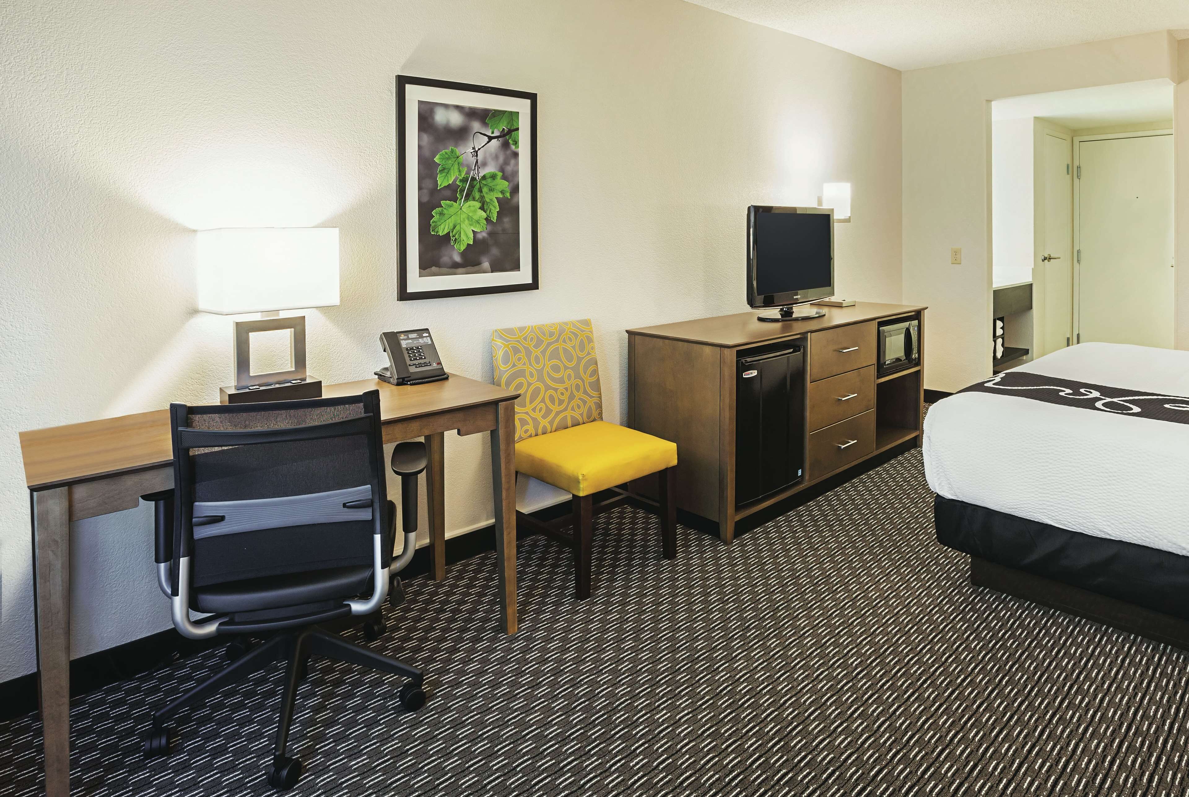 A hotel room with a desk, chair, television, bed, and a framed picture on the wall.