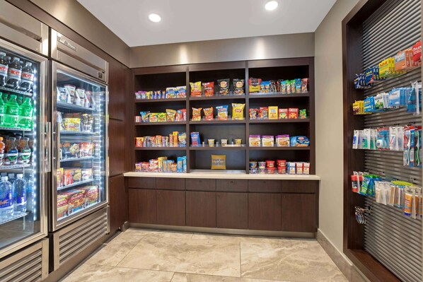 Zona de autoservicio con aperitivos y bebidas, que incluye bebidas refrigeradas, estantes con bocadillos y productos envasados, además de un suelo limpio y con baldosas.