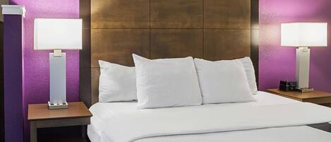 Una habitación de hotel con una cama grande, dos mesitas de noche con lámparas y un cabecero de madera.