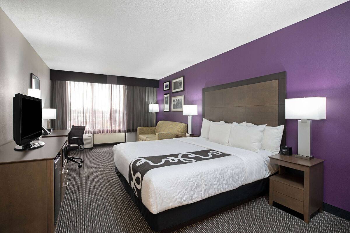 A hotel room with a large bed, a desk with a computer, a chair, and a TV.