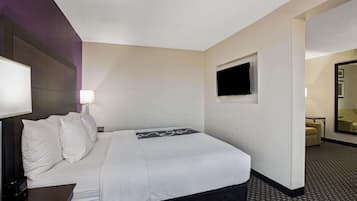 A hotel room with a bed, a TV mounted on the wall, and a desk with a lamp.