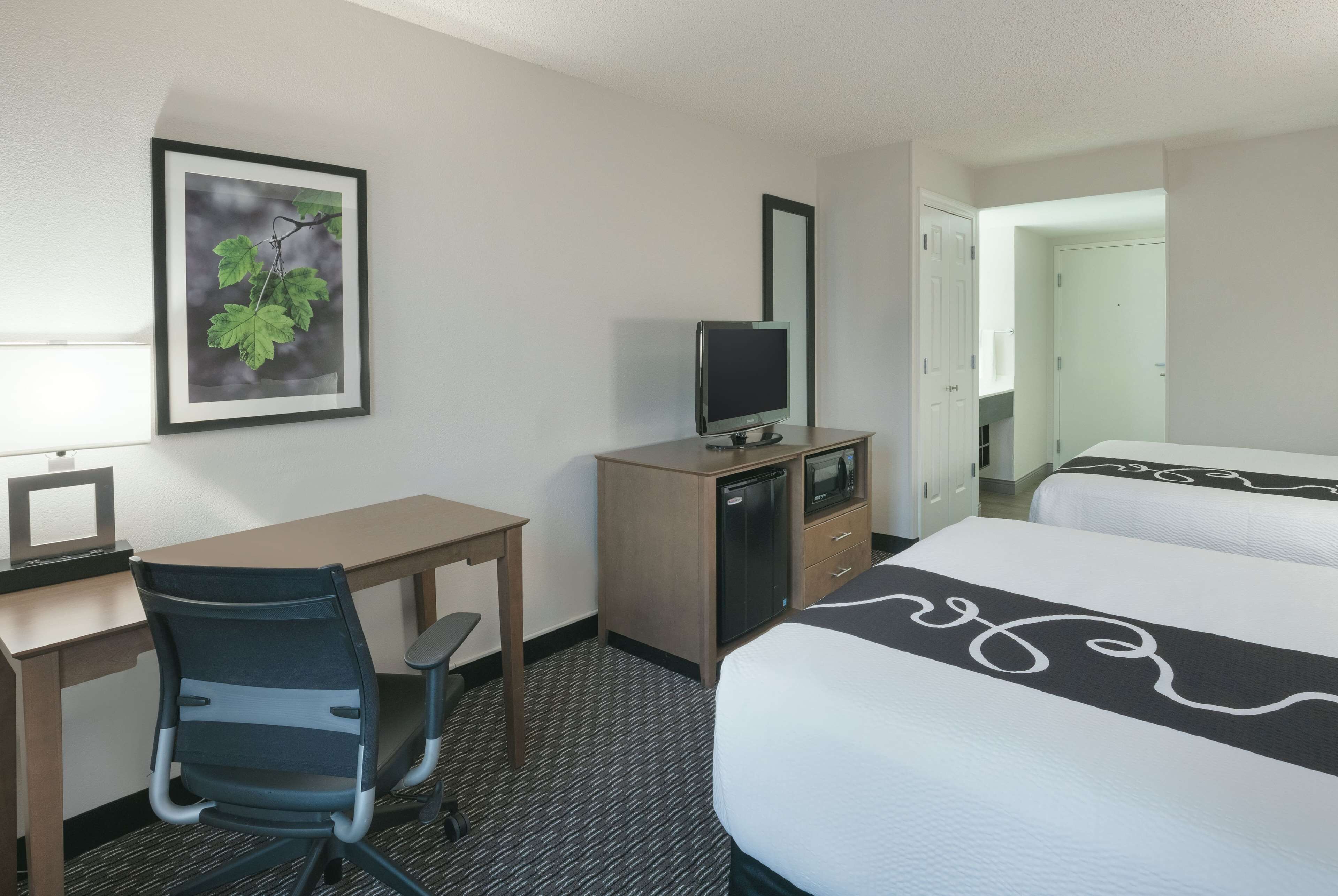 A hotel room with a bed, a desk with a chair, a television, and a framed picture on the wall.