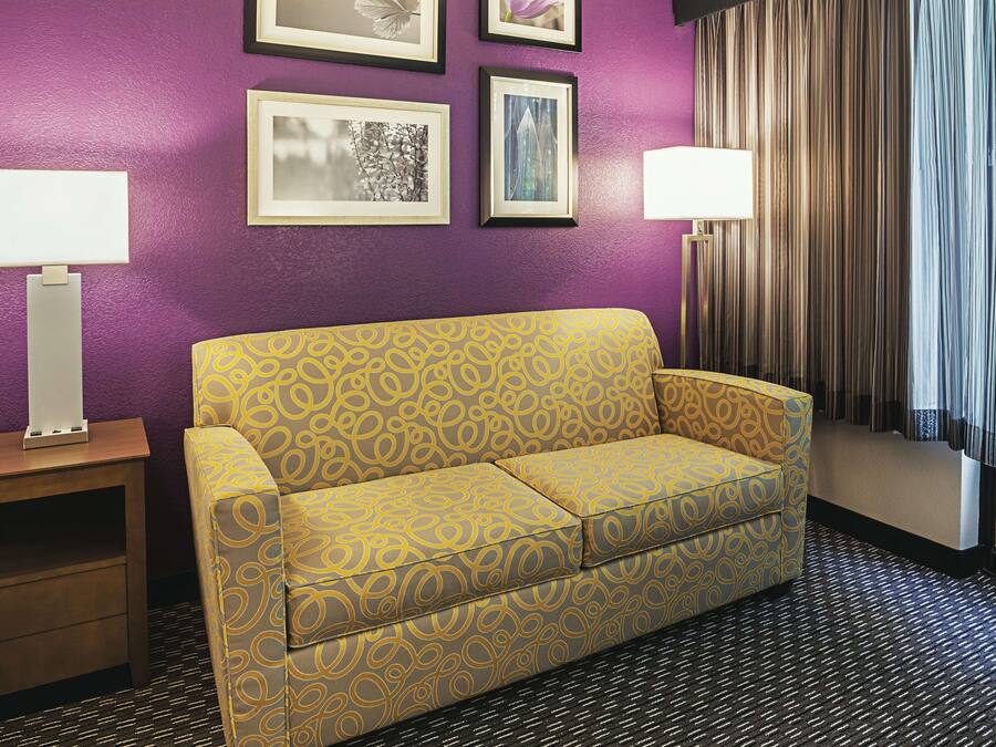 A room with a purple wall, a yellow patterned sofa, two bedside tables with lamps, and framed pictures on the wall.