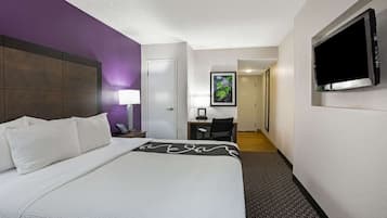 Una habitación de hotel con una cama grande, un escritorio, una silla, un televisor y una puerta que da a un pasillo.