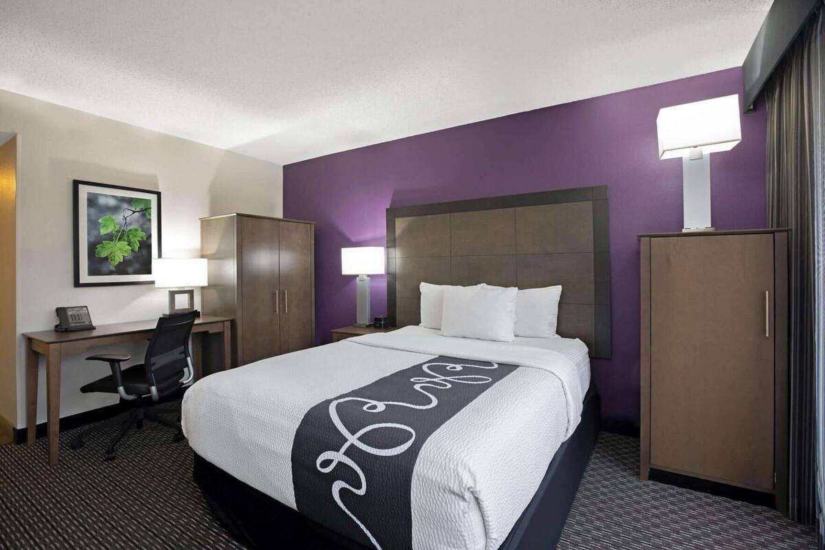 A hotel room with a bed, desk, chair, and wardrobe.
