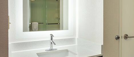 A bathroom with a white countertop, a sink, and a mirror above it.