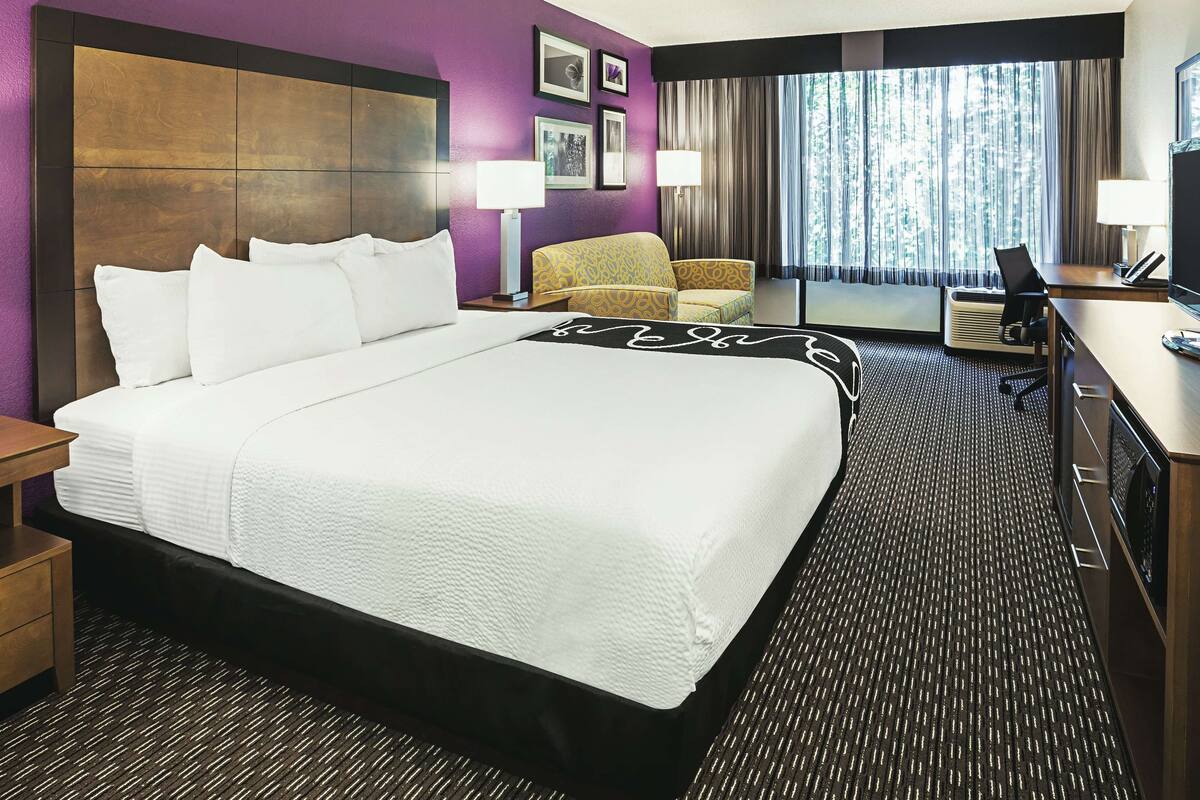 A hotel room with a large bed, a sofa, a desk, and a view of the outdoors through a window.