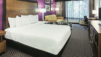 A hotel room with a large bed, a sofa, a desk, and a view of the outdoors through a window.