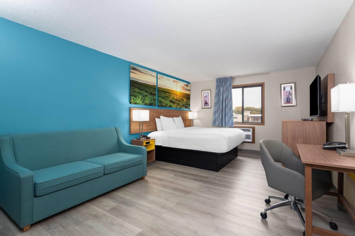 A hotel room with a bed, a desk, a chair, a sofa, and a painting on the wall.