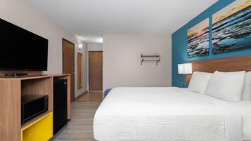 A hotel room with a bed, a TV, a small kitchenette, and a hallway leading to another room.