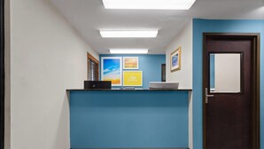 A reception area with a blue counter, a computer, framed pictures on the wall, and a door. - Days Inn by Wyndham Austin (Austin)