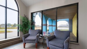 A room with two patterned armchairs, a small round table, and a large window with a view of a building and greenery. - Days Inn by Wyndham Austin (Austin)
