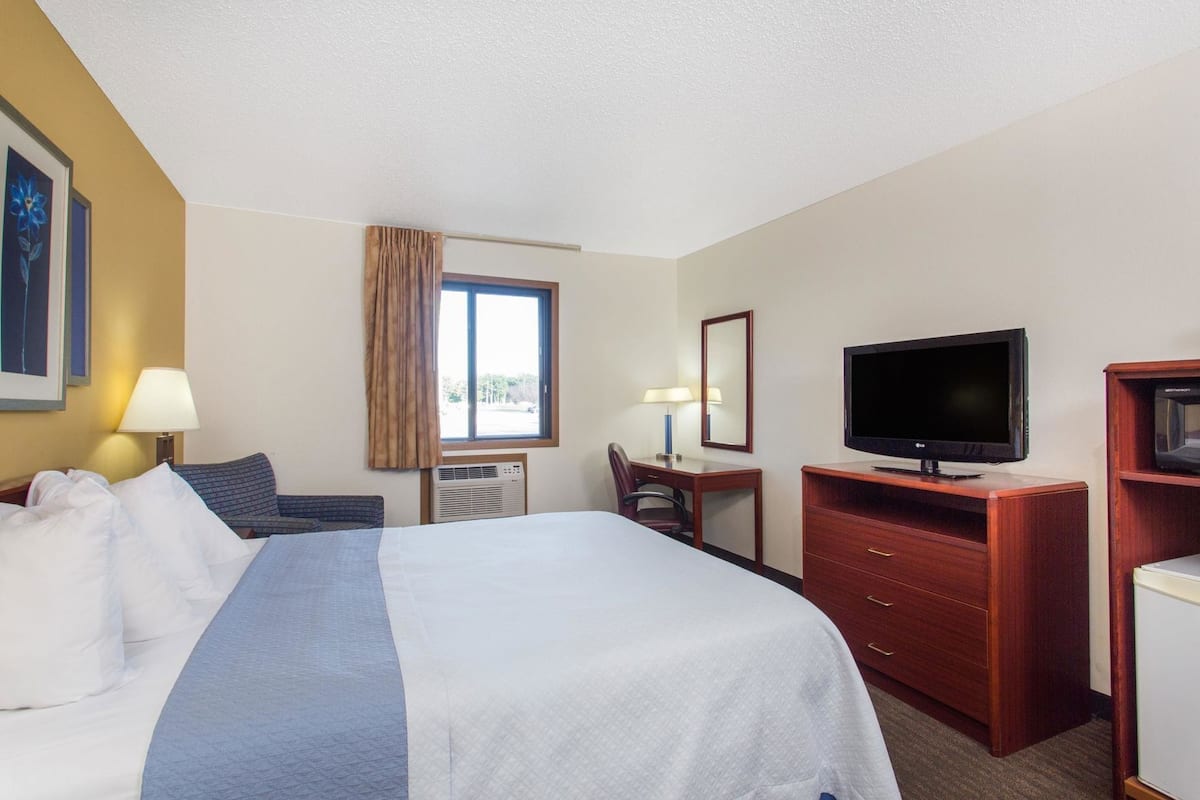 A hotel room with a bed, a desk, a television, and a dresser.