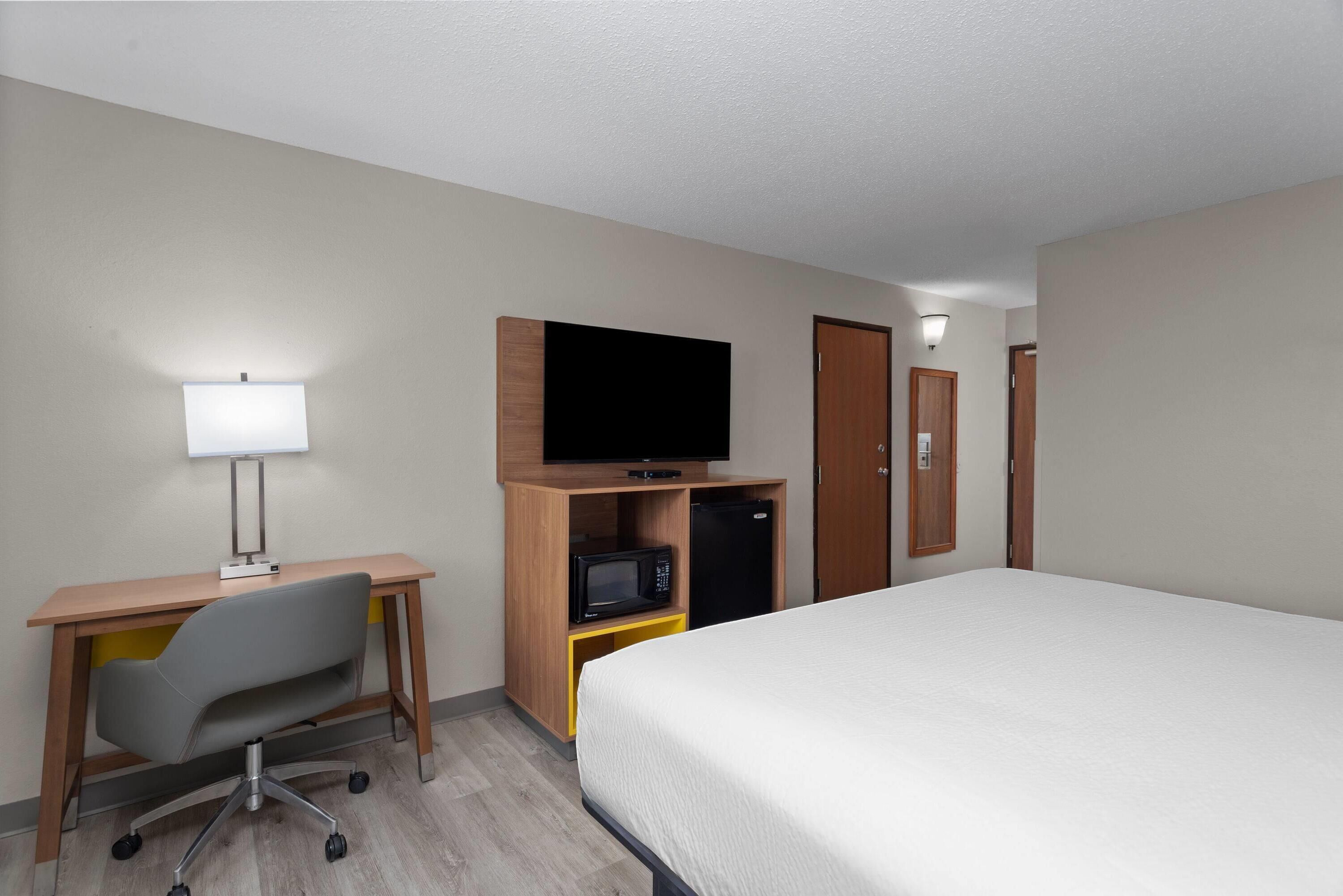 Habitación de hotel con cama, escritorio con silla, televisor, microondas y armario.