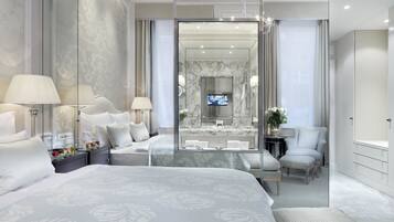 A modern hotel room with a large bed, a sitting area with a glass partition, a bathroom with a marble vanity, and a television in the mirror.