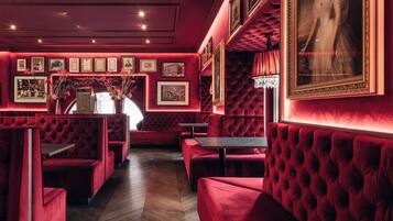 Un restaurante tenuemente iluminado con cabinas y mesas de terciopelo rojo, cuadros en las paredes y un candelabro.