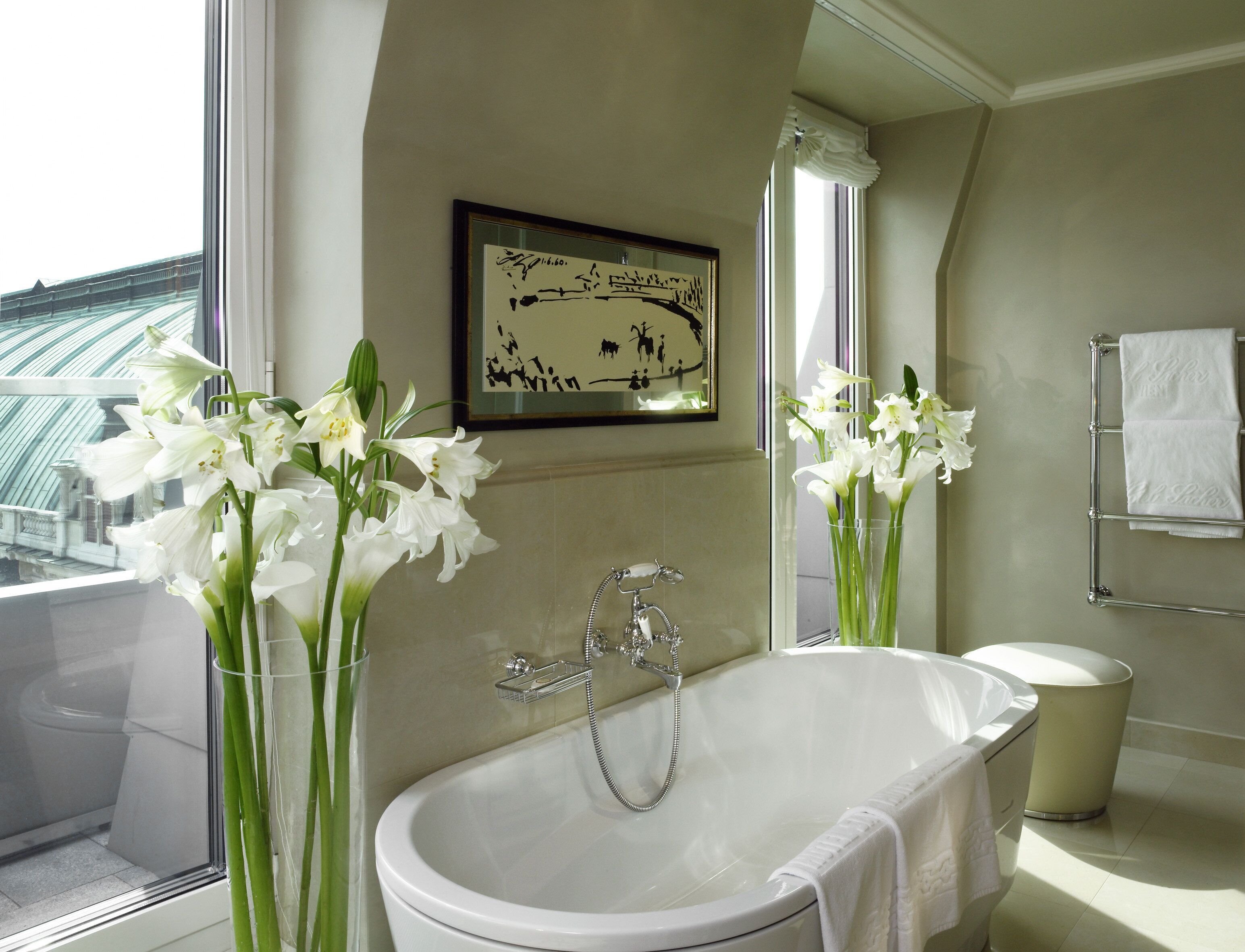 A modern bathroom with a bathtub, a window with a view of a bridge, and two vases with white flowers.
