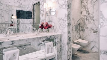 A modern bathroom with marble walls, a large mirror, a vanity with a sink, and a toilet.