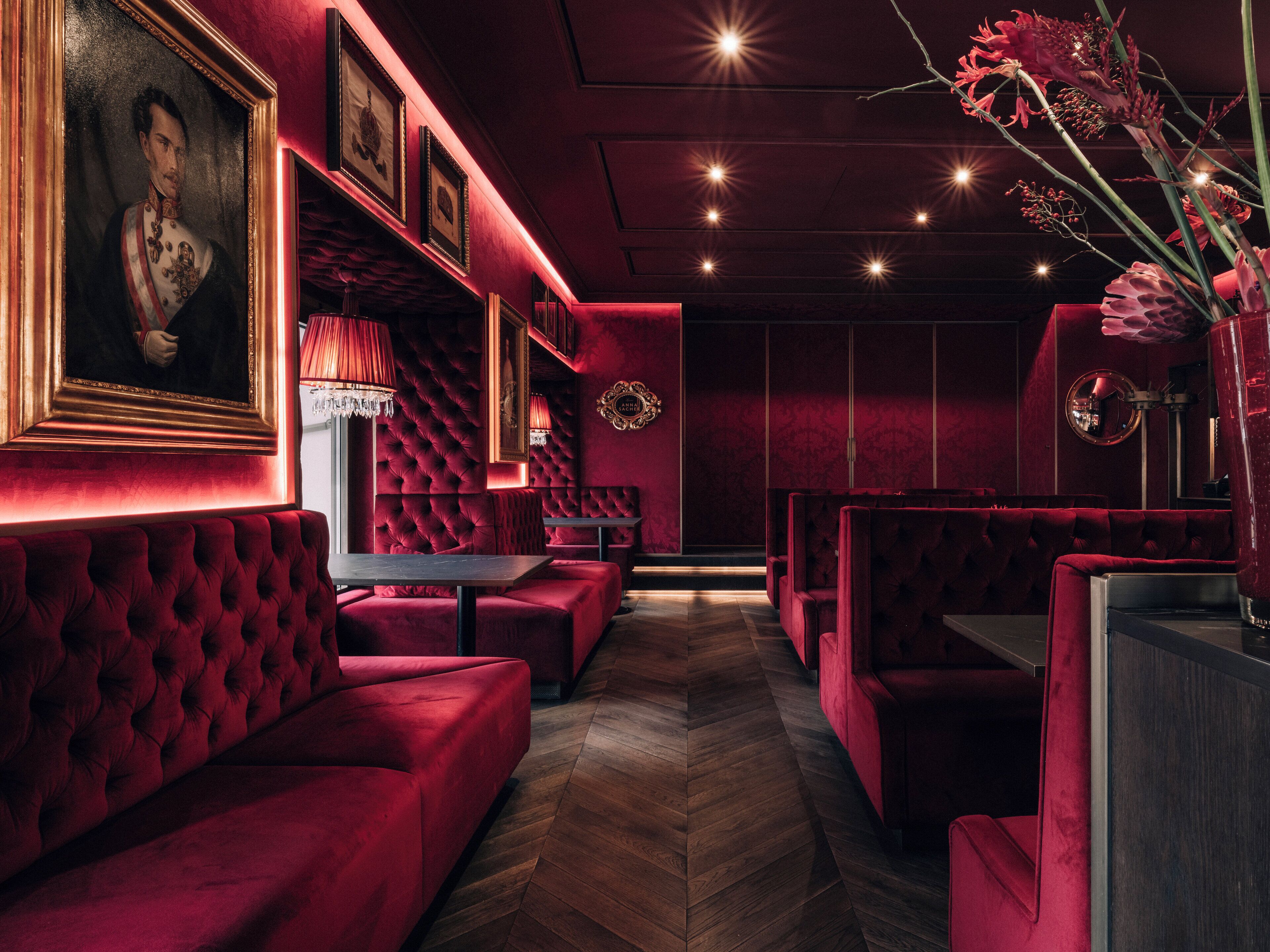 A dimly lit room with red velvet seating, framed portraits, and a chandelier.