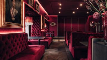 A dimly lit room with red velvet seating, framed portraits, and a chandelier.