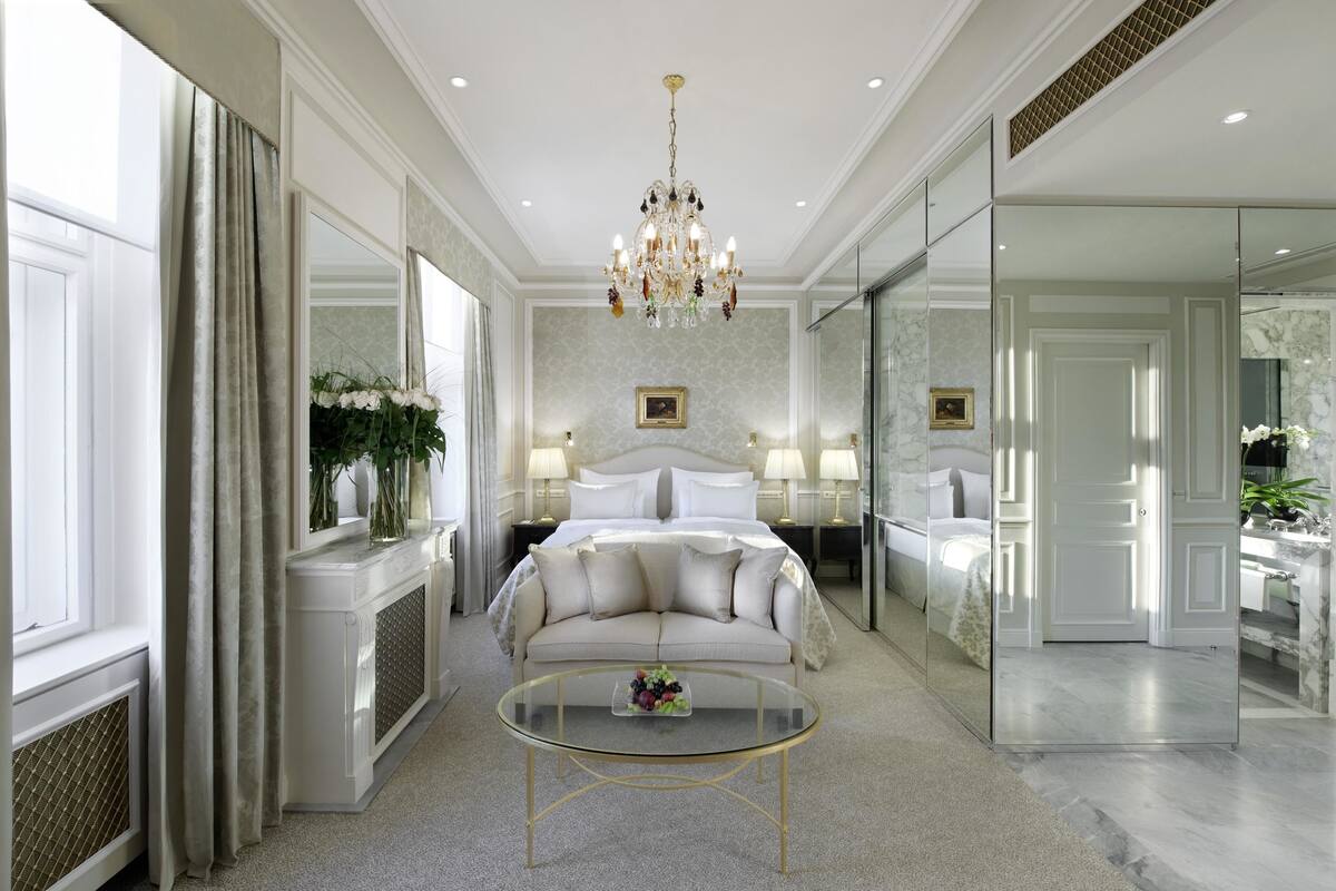 Ein luxuriöses Schlafzimmer mit einem großen Bett, einem Glastisch und einer Chandelieber.
