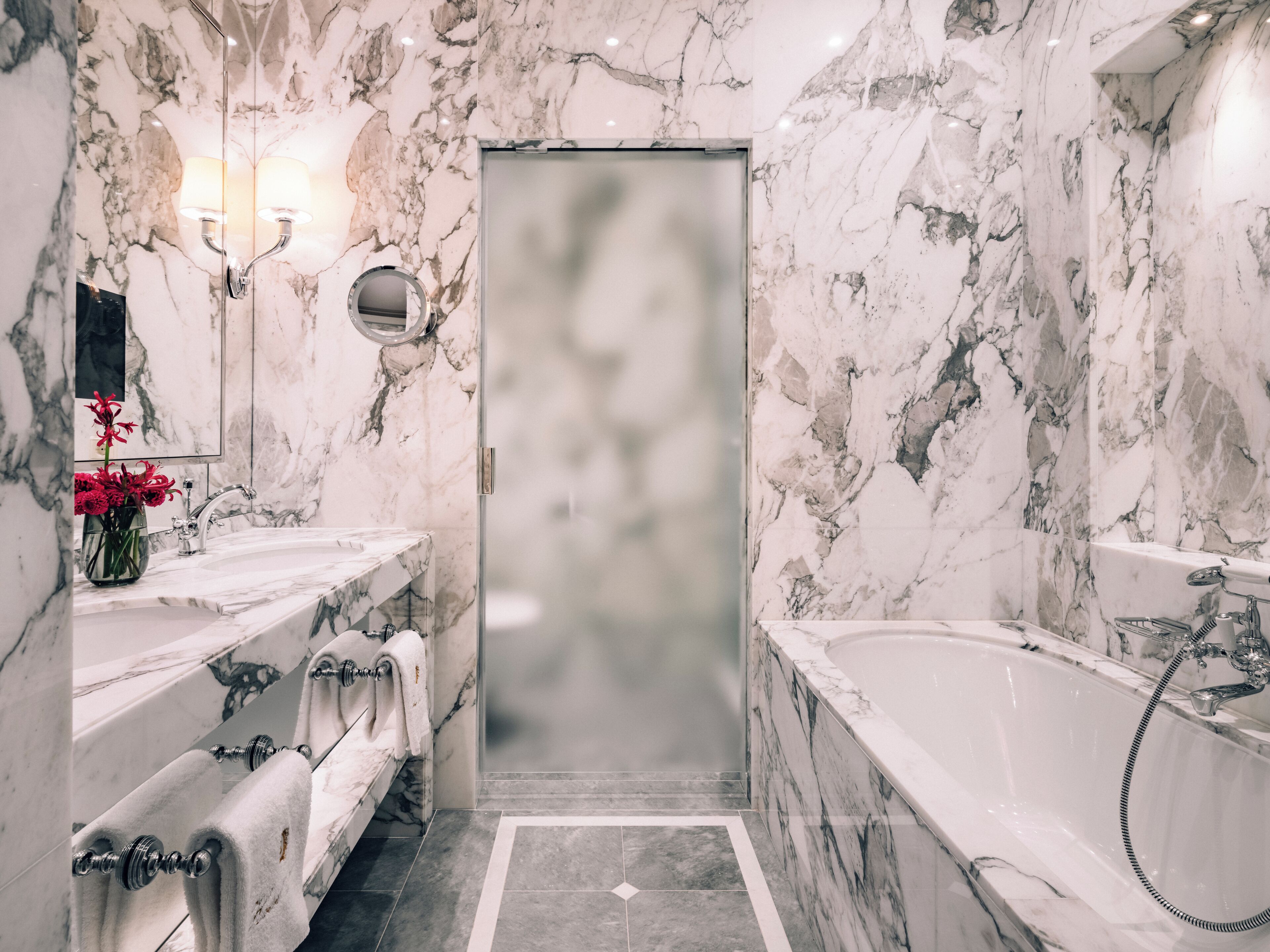 Un baño con paredes de mármol, una bañera grande y dos lavamanos.