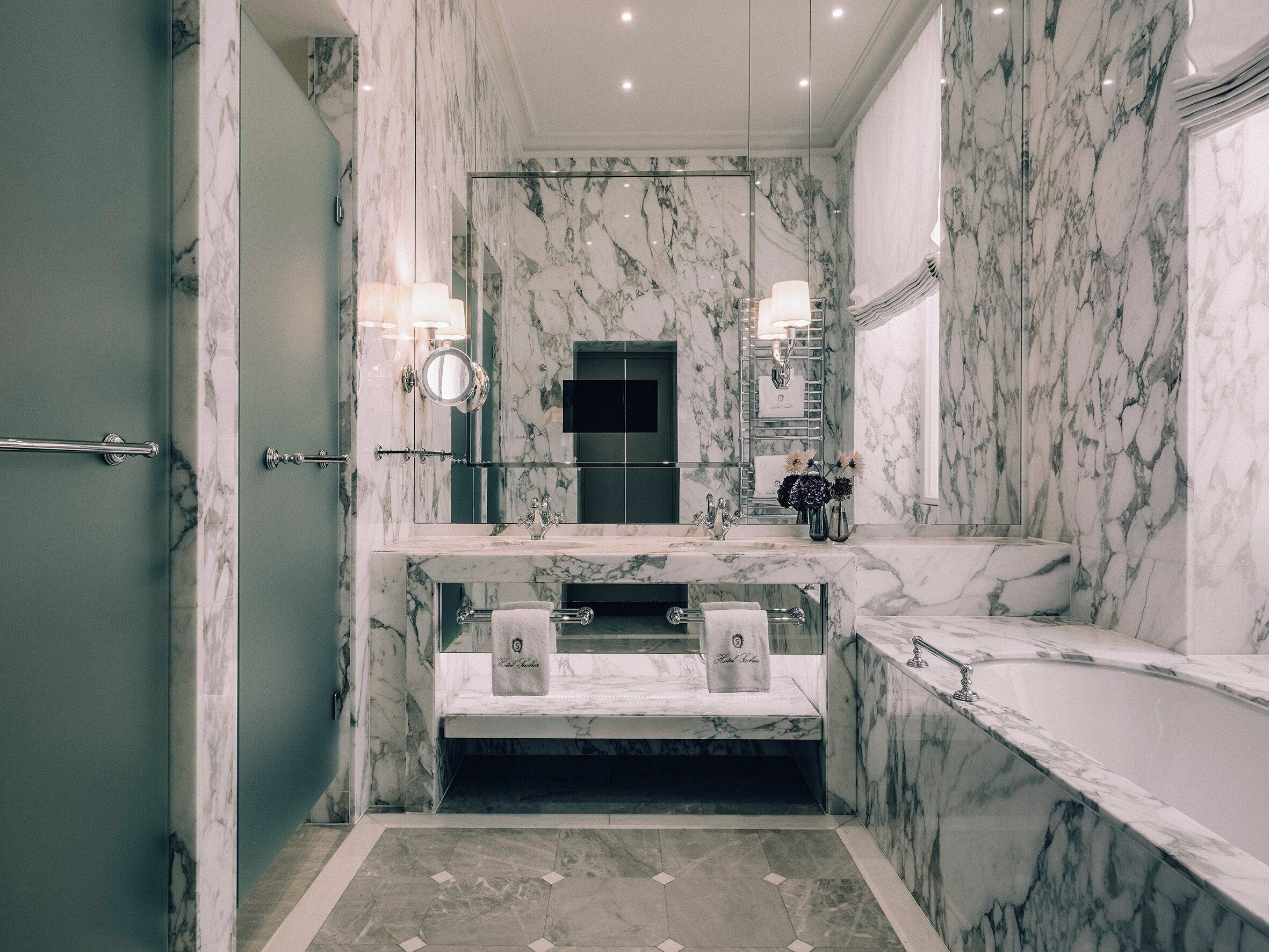 A luxurious bathroom with marble walls, a large mirror, a bathtub, and a vanity with a sink and towel rack.