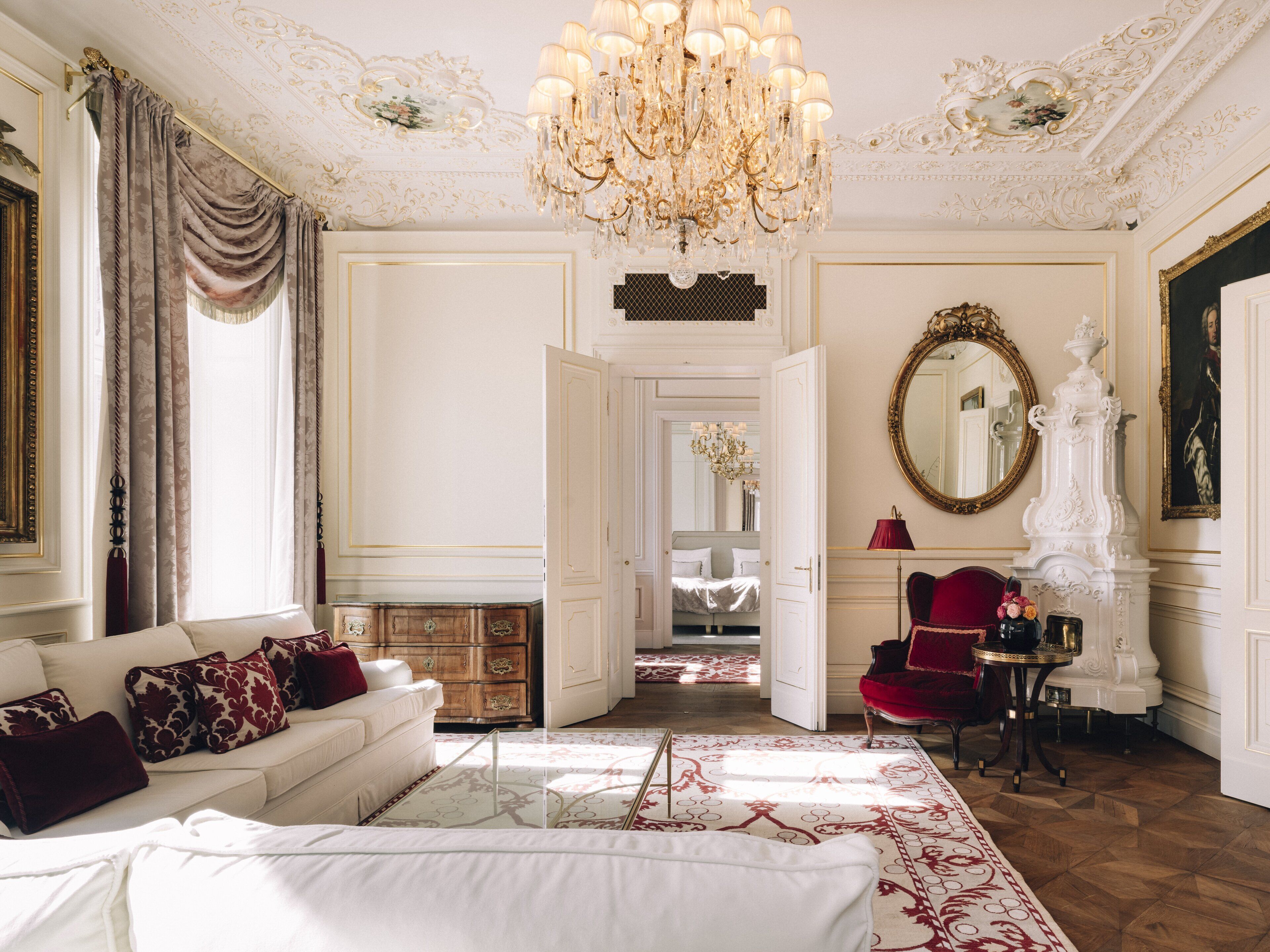 Um quarto luxuoso com um sofá branco, uma poltrona vermelha e um grande lustre.