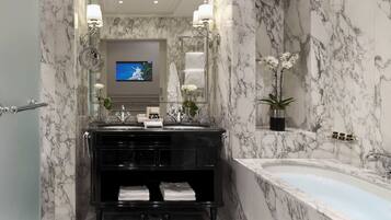 A bathroom with a marble vanity, a bathtub, and a television screen.
