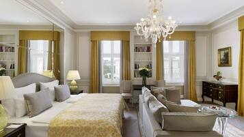 A spacious hotel room with a large bed, a sofa, a desk, and a chandelier.