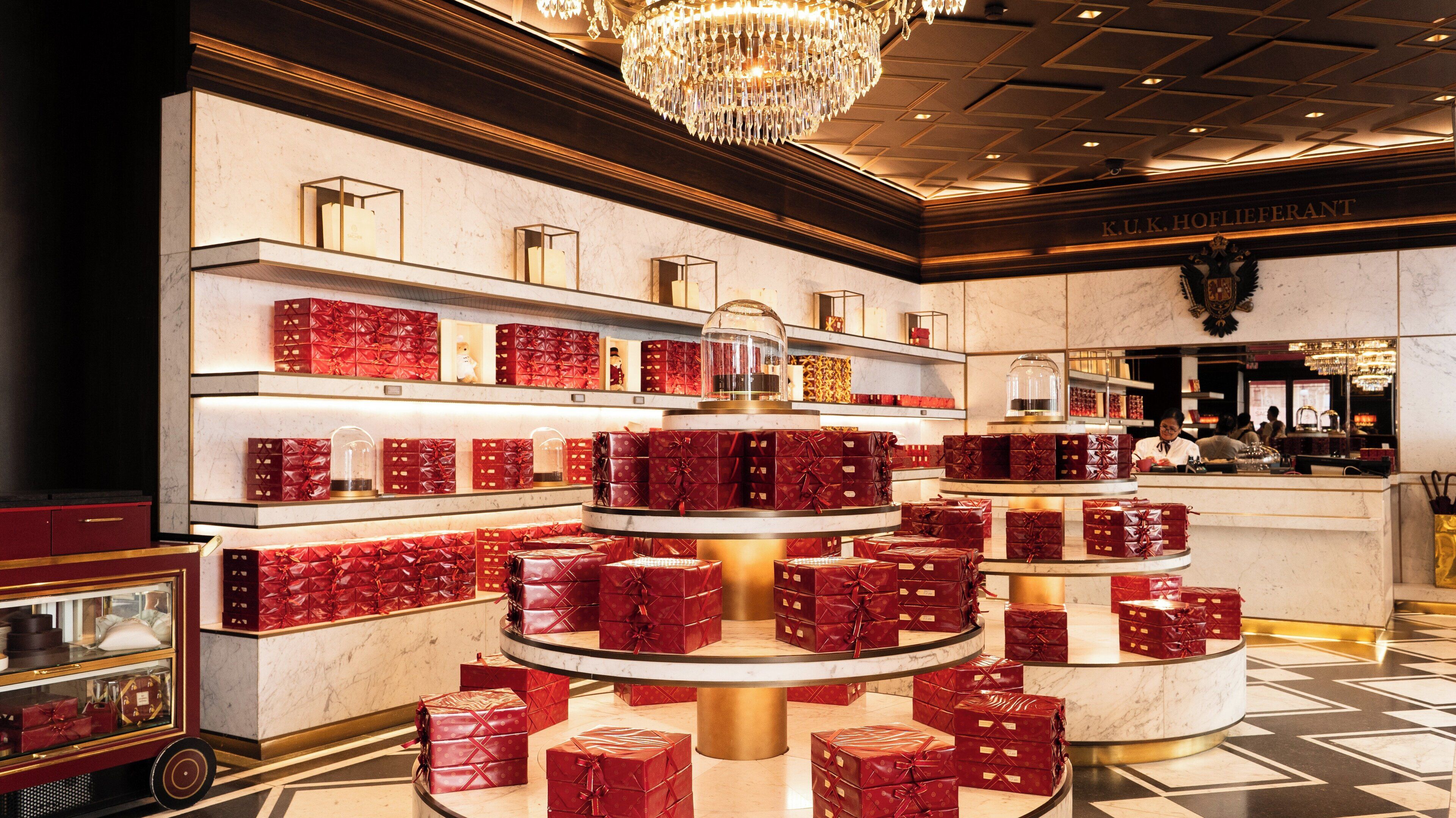 A luxurious hotel lobby with a central display of red gift boxes, marble walls, and a chandelier.