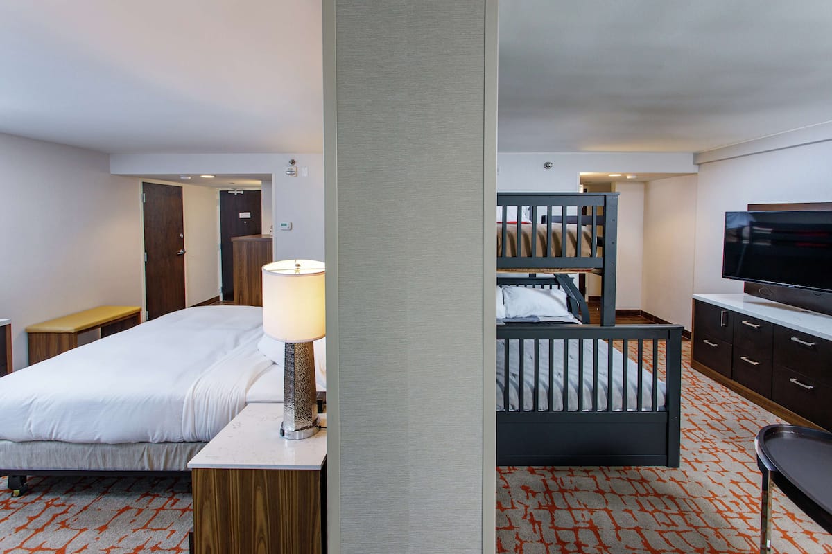 Una habitación de hotel con cama, escritorio con lámpara, televisión, litera y armario.