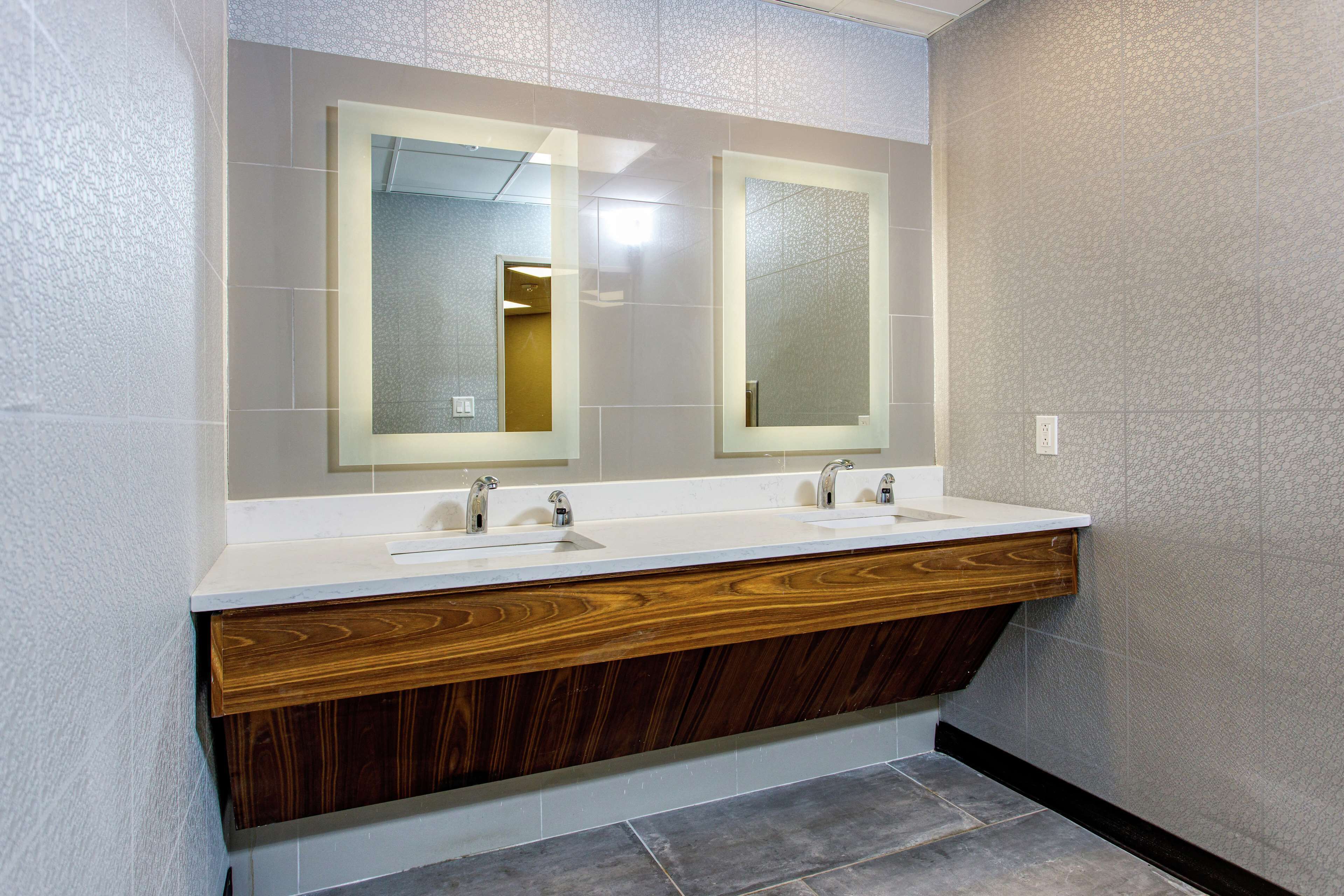 Un baño moderno con dos lavamanos, tocador de madera y espejos grandes.