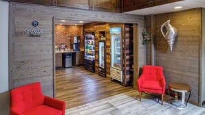 A lobby with a wooden wall, a red armchair, a second red armchair, a small round table, and a vending machine. - DoubleTree by Hilton Appleton (Appleton)