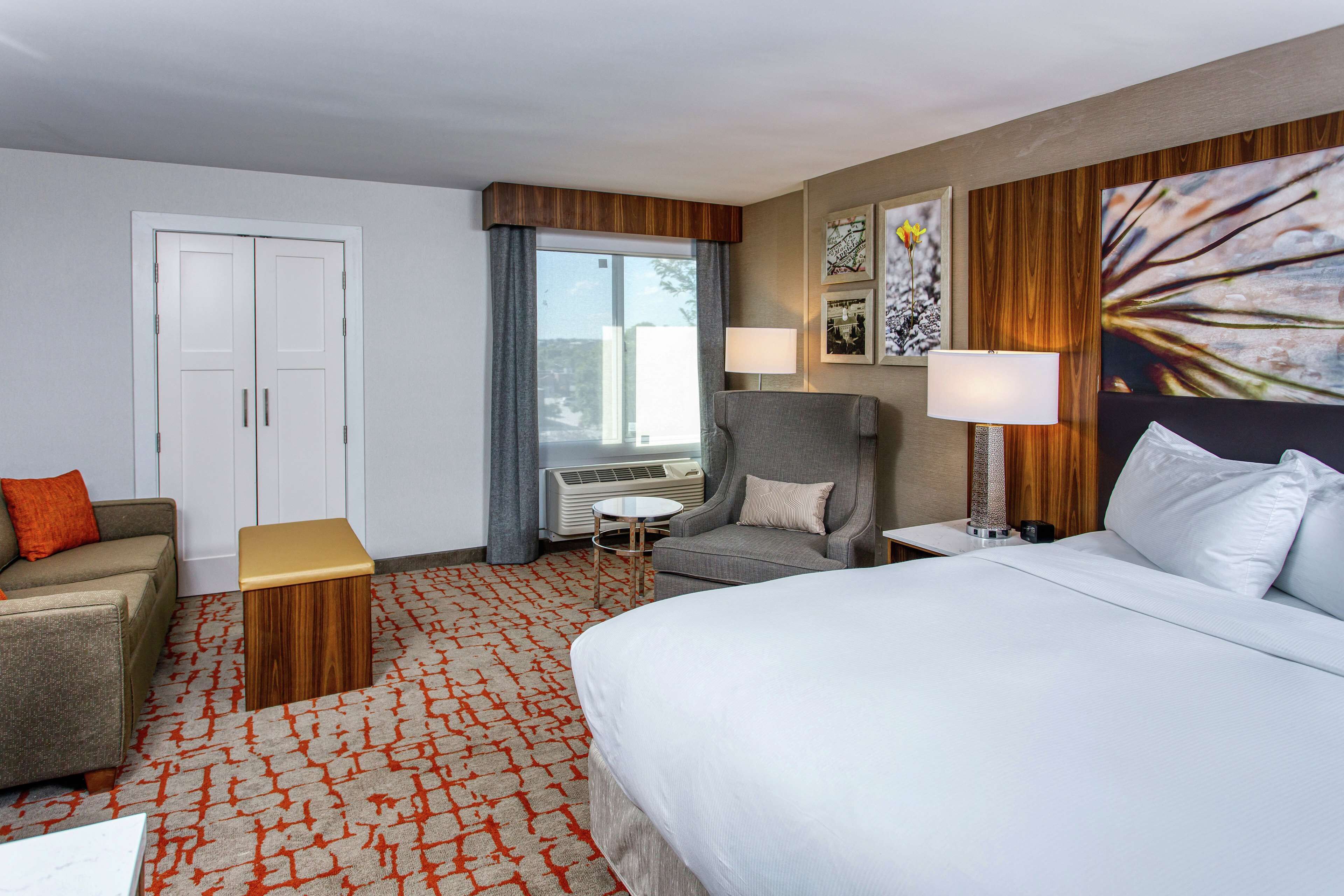 Una habitación de hotel con cama, sofá, sillón, mesita y ventana con cortinas.
