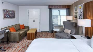 A hotel room with a bed, a sofa, a desk, a chair, and a window with a view.