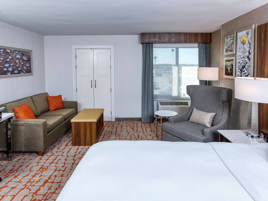 A hotel room with a bed, a sofa, a desk, a chair, and a window with a view.