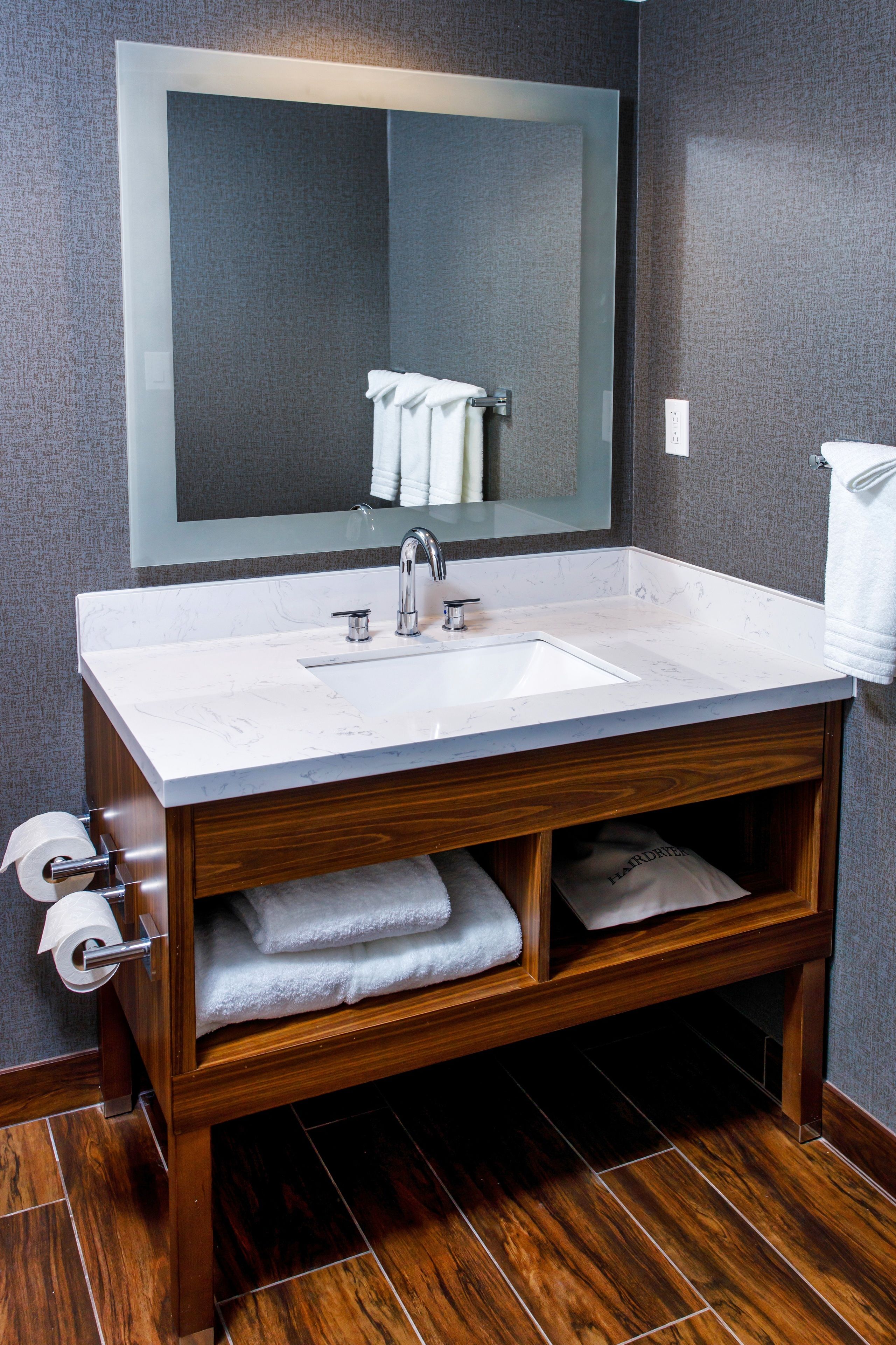 A modern bathroom with a marble sink, wooden vanity, and a large mirror.