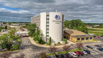 Un hotel con un llamativo letrero de 'DoubleTree by Hilton', un estacionamiento y edificios circundantes.