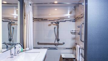 Une salle de bain moderne avec un grand miroir, deux lavabos, une douche équipée de barres d’appui et un porte-serviettes.