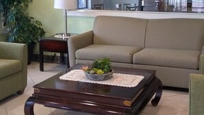 A living room with a sofa, a coffee table with a plant, a lamp, and a large window with artwork. - Quality Inn Little Creek (Virginia Beach)