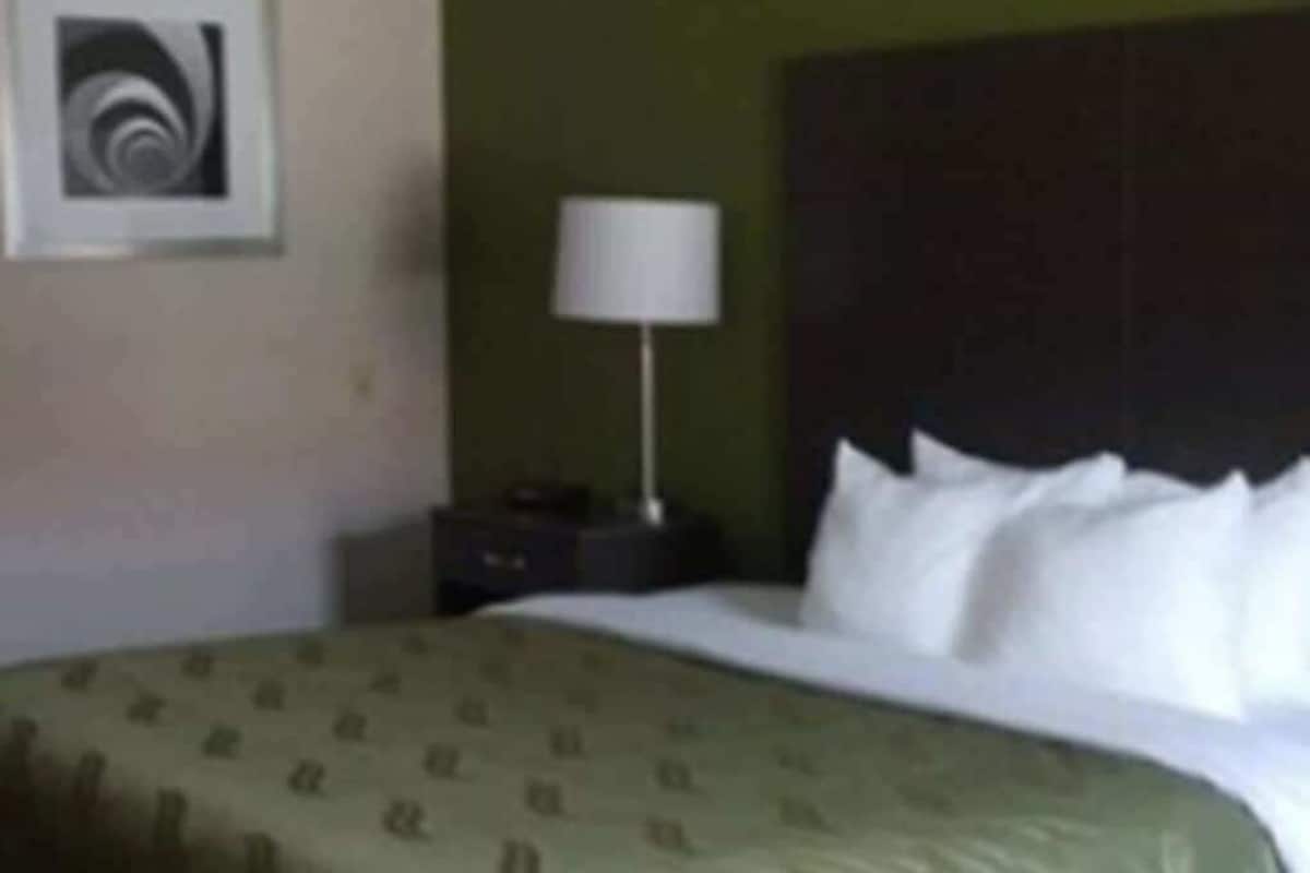 A hotel room with a bed, a nightstand, a lamp, and a framed picture on the wall.