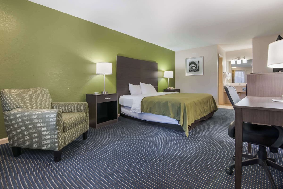 A hotel room with a bed, a desk, a chair, and a nightstand.