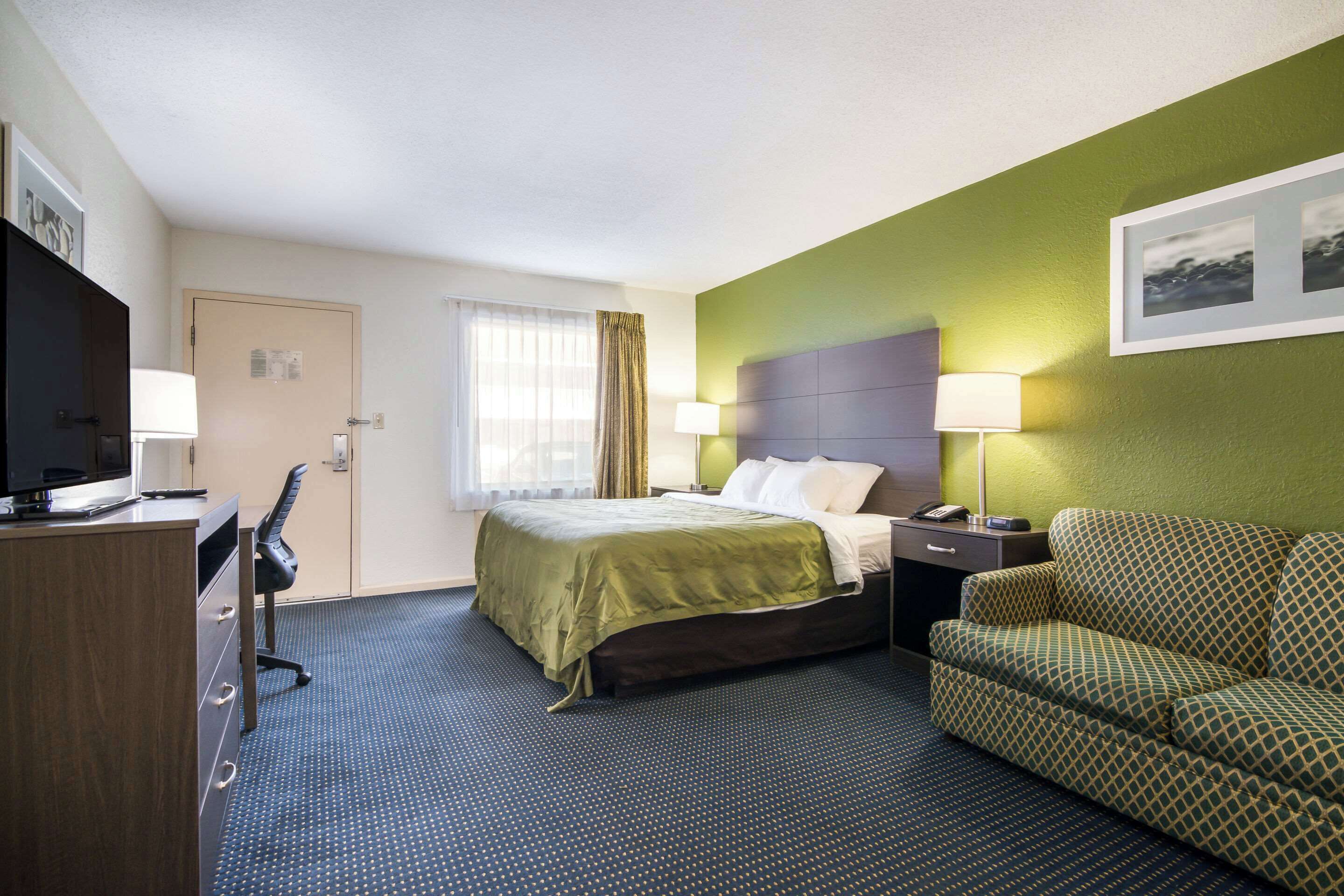Una habitación de hotel con cama, escritorio, sillón, sofá y televisor.