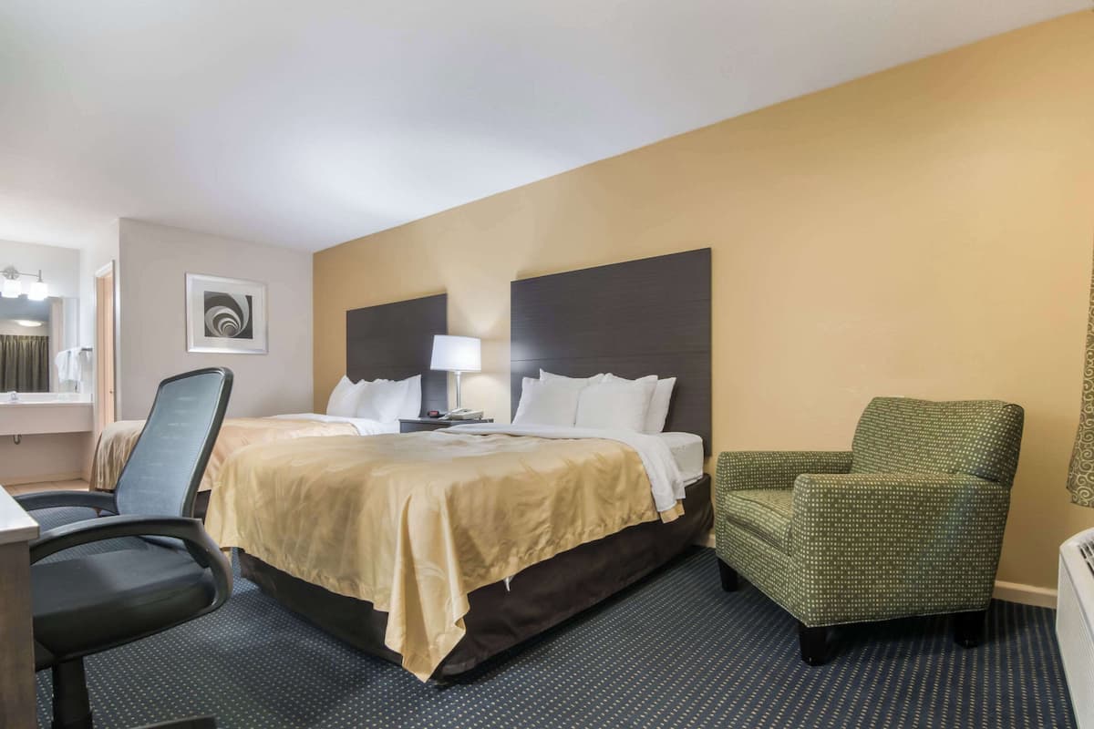 A hotel room with a bed, a desk, a chair, a lamp, and a wall art piece.