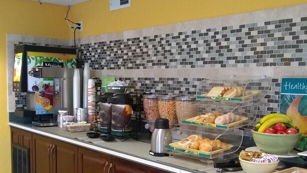 A breakfast bar with a coffee machine, cereal, and fruit bowls. - Quality Inn Little Creek (Virginia Beach)