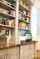 A kitchen with marble countertops, a laptop on the counter, and a bookshelf filled with books and decorative items.