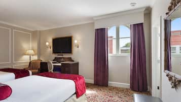 Une chambre d’hôtel avec deux lits, un bureau, une chaise, une télévision et une grande fenêtre avec des rideaux.