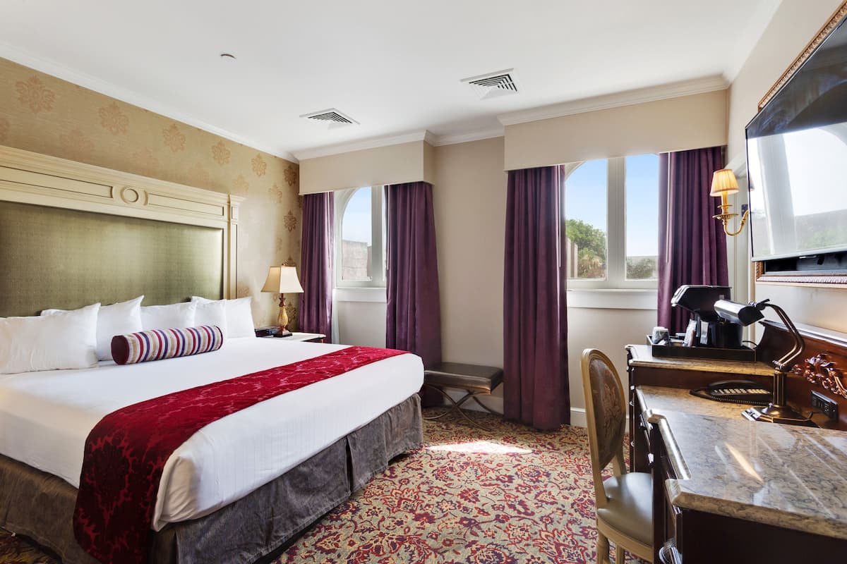 A hotel room with a large bed, a desk with a chair, a television, and a window with curtains.